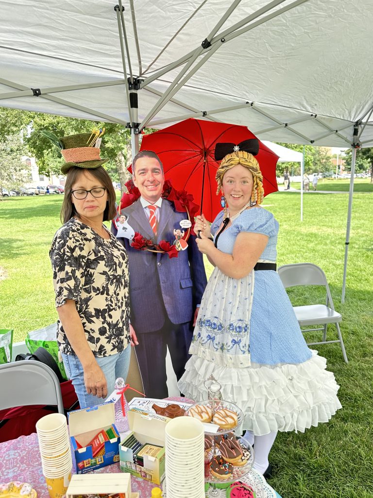 Women dressed as the Mad Hatter and Alice in Wonderland flank a cardboard cut out of Congressman Gabe Evans at Greeley Protest